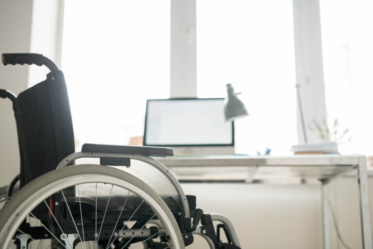 Rollstuhl in einem modernen Büro mit Schreibtisch und Computer im Hintergrund, symbolisiert Barrierefreiheit und inklusives Arbeiten.