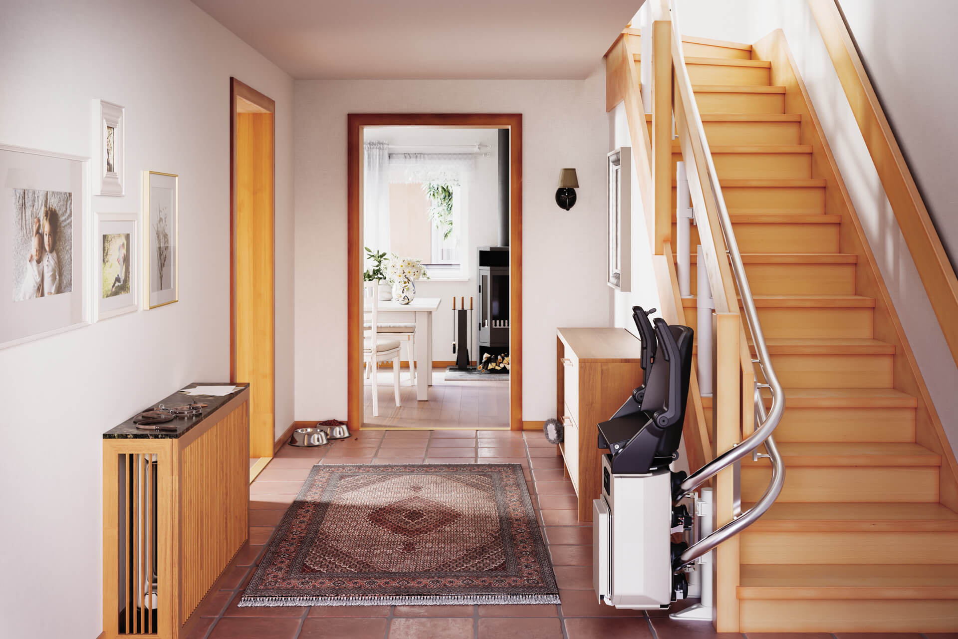 Helles und einladendes Treppenhaus mit Holztreppe, modernem Handlauf und einem Treppenlift. Im Vordergrund ein stilvoller Teppich und ein Holzsideboard, während im Hintergrund ein Essbereich mit Tisch und Stühlen zu sehen ist. Die Wände sind mit Familienfotos dekoriert, und es gibt einen Kamin sowie Futternäpfe für Haustiere.