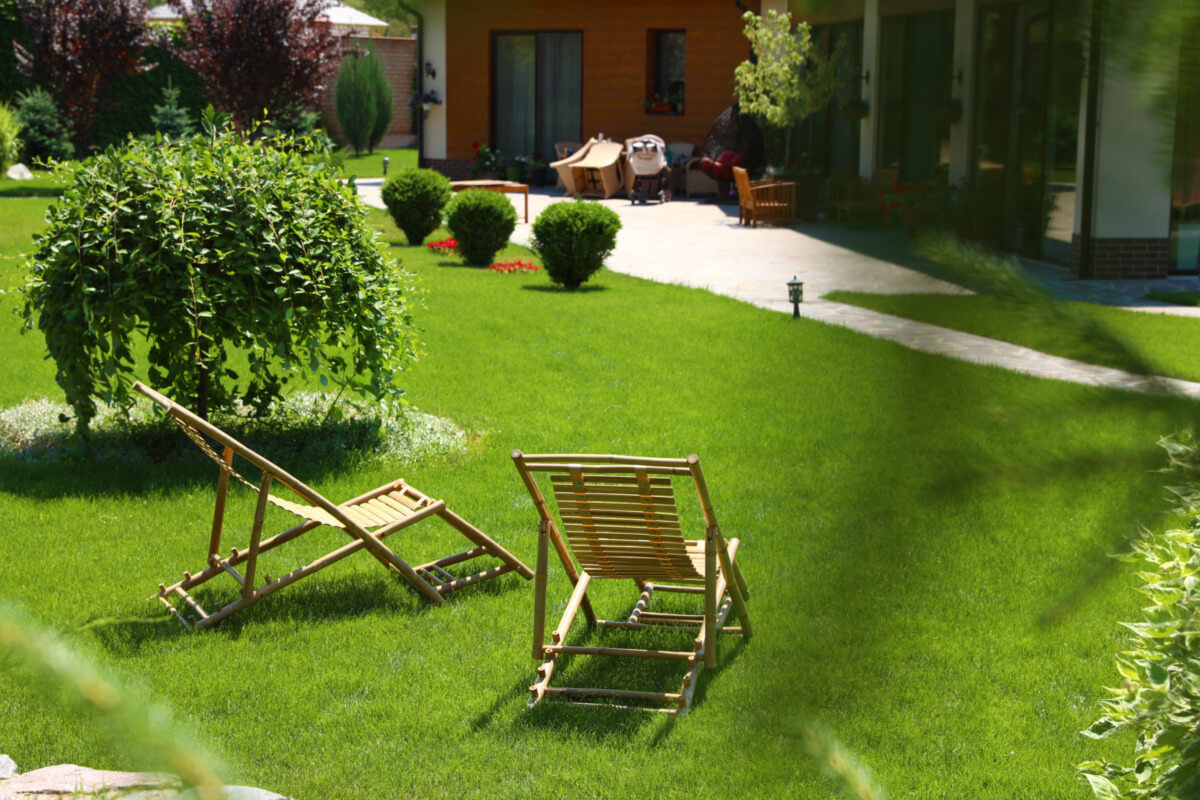 Gemütlicher Garten mit grünem Rasen, zwei Holzliegestühlen und einem gepflegten Strauch im Hintergrund, ideal für Entspannung und Freizeitaktivitäten.
