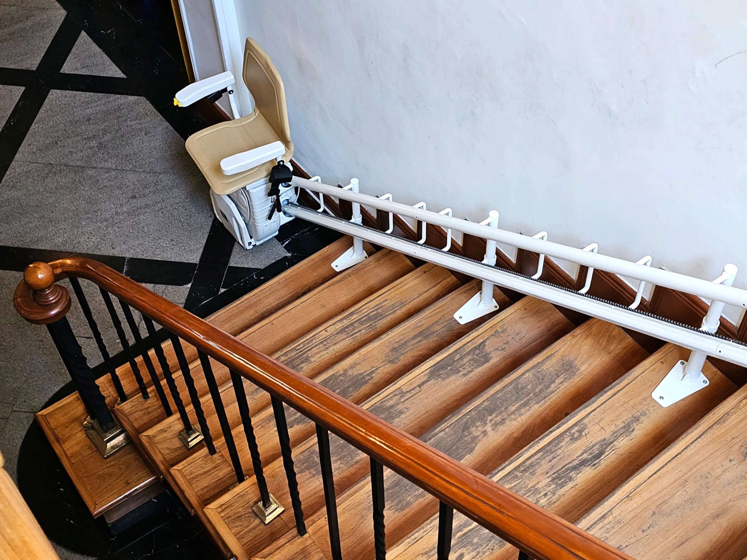 Treppenlift auf einer Holztreppe mit einem gelben Sitz und einer weißen Schiene für barrierefreies Wohnen, der eine sichere und einfache Nutzung der Treppe ermöglicht.