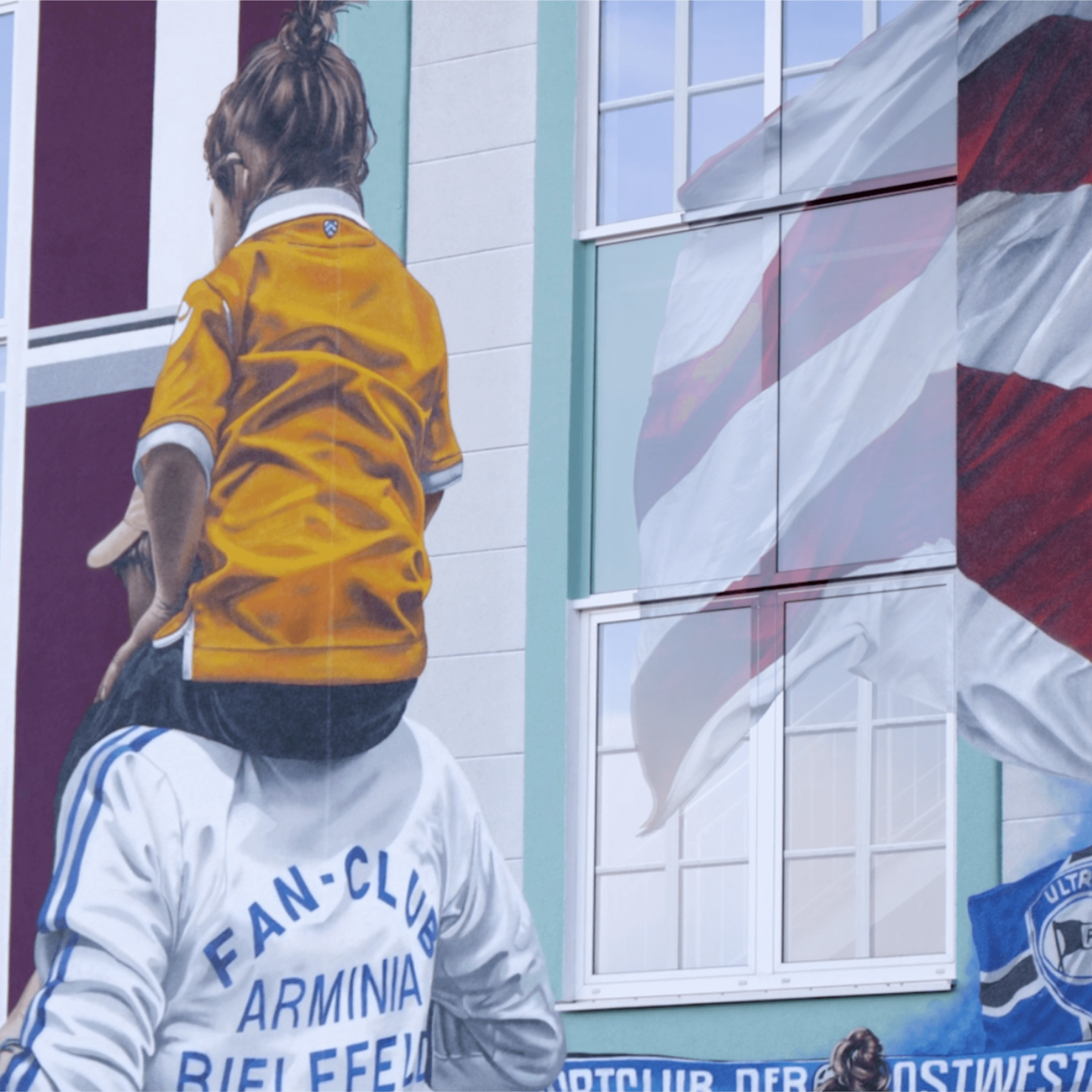 Mural eines Kindes in einem orangefarbenen Trikot, das auf den Schultern eines Erwachsenen sitzt. Im Hintergrund sind Fenster und eine Flagge zu sehen, die die Verbundenheit mit dem Fanclub Arminia Bielefeld symbolisieren.