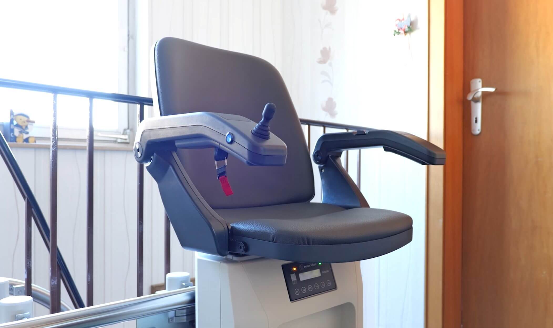 Treppenlift mit ergonomischem Sitz und Joystick-Bedienung, ideal für barrierefreies Wohnen, vor einem Fenster in einem hellen Raum.