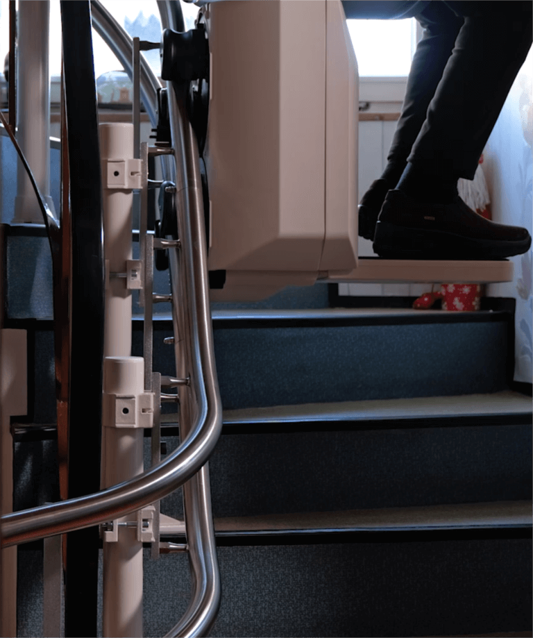 Bild eines Treppenlifts, der eine Person beim Aufstieg auf einer Treppe unterstützt, mit Fokus auf die Treppenstufen und das Sicherheitsgeländer. Der Treppenlift ist modern und dient der Barrierefreiheit in Wohnräumen.