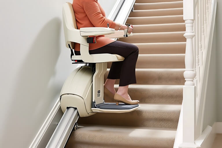 Frau sitzt auf einem Treppenlift, der eine Treppe hinunterfährt, und sorgt für barrierefreies Wohnen. Der Lift ist beige und verfügt über einen stabilen Sitz sowie eine Fußablage.